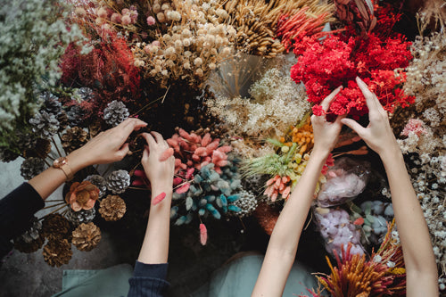 Lots of dried flowers being worked with by two pairs of hands