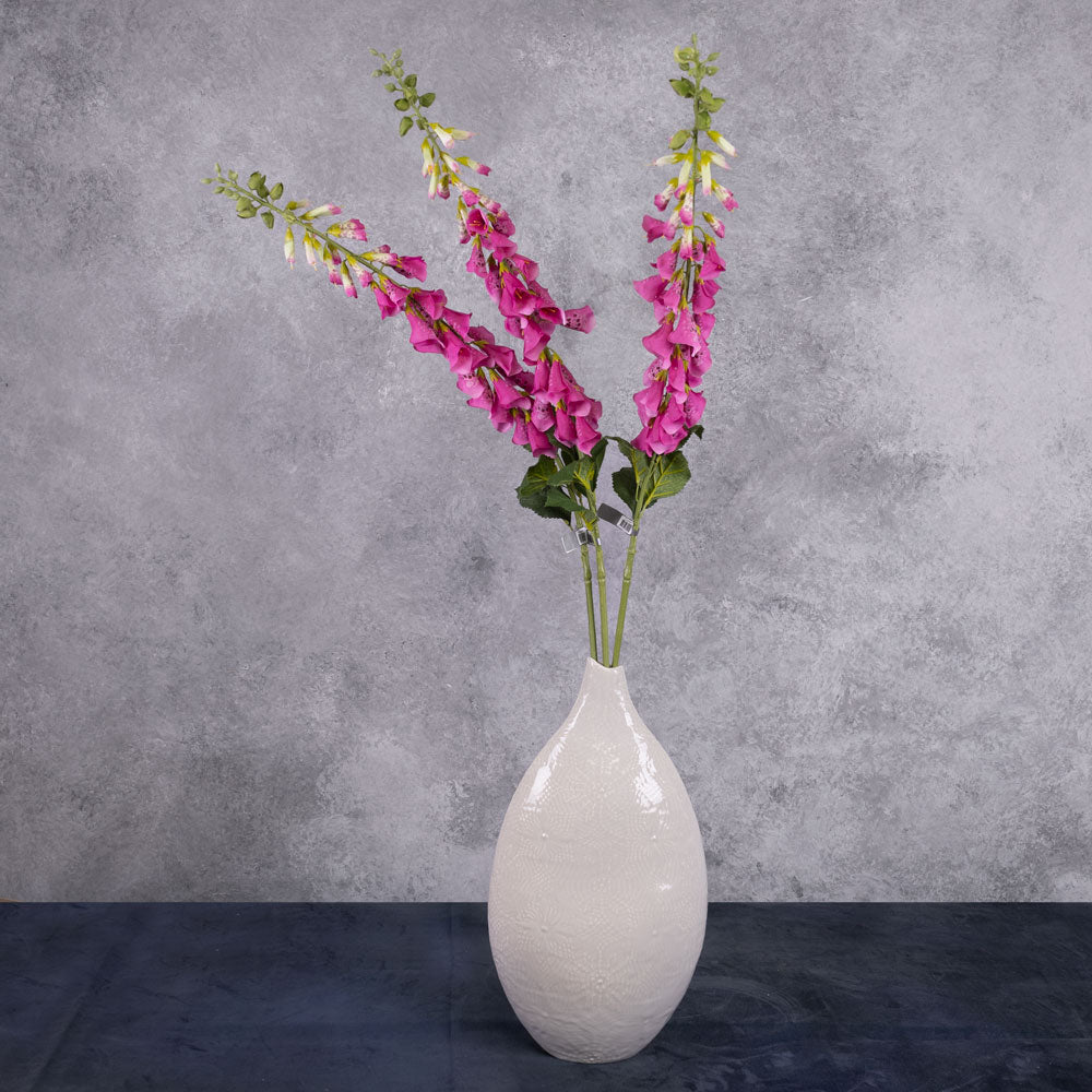 3 individual stems of fuchsia coloured, faux fox gloves in a cream coloured oval vase