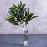 A faux mango bush stem showing lots of deep green leaves, displayed in a clear glass vase