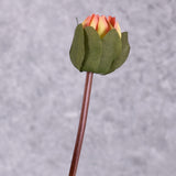 A close up of a faux dahlia bud with the orange-red colour peeking through the foliage